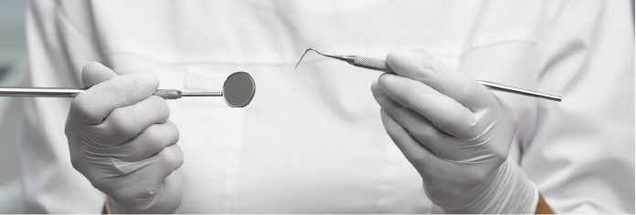 Le mani di un odontoiatra con guanti reggono specchietto e sonda